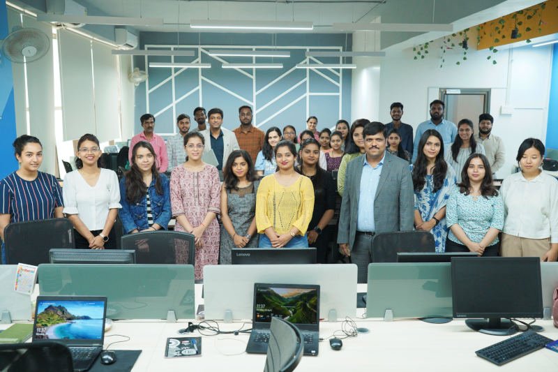 A diverse group of individuals standing in front of computer screens, engaged in a collaborative work environment.