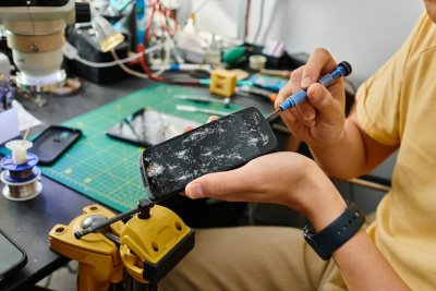 Technician disconnecting broken touchscreen of mobile phone with screwdriver.