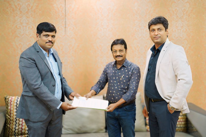 Three men standing in front of a couch, holding a piece of paper.